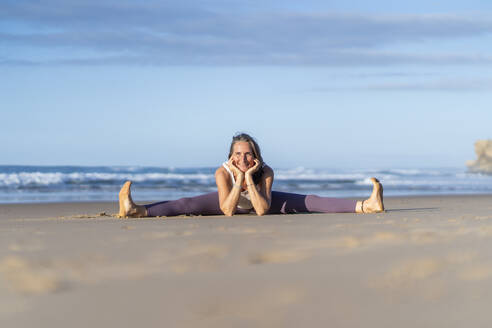 Lächelnde Frau, die am Strand die Yoga-Pose der Grätsche übt - JSIF00020