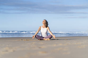 Woman practicing Lotus position sitting on sand at beach - JSIF00022