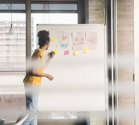 Young businesswoman writing on adhesive note in office - UUF31603