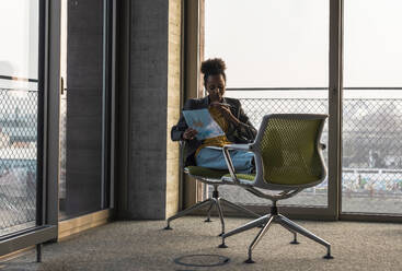 Businesswoman sitting on chair and talking on smart phone in office - UUF31607