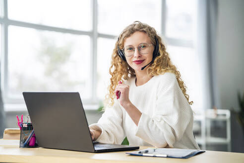 Smiling saleswoman wearing headset near laptop in office - MDOF01839