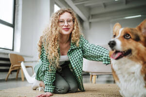 Smiling woman sitting with dog on floor at home - MDOF01842