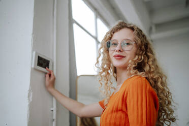 Smiling woman near thermostat on wall at home - MDOF01853