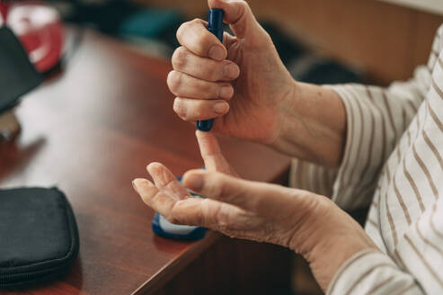 Ältere Frau sticht sich in den Finger, um den Blutzuckerspiegel zu Hause zu messen - ANAF02731