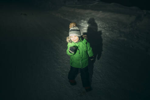 Verspielter Junge steht nachts im Schnee - ANAF02734