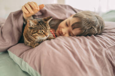 Junge auf dem Bett liegend mit Katze zu Hause - ANAF02735