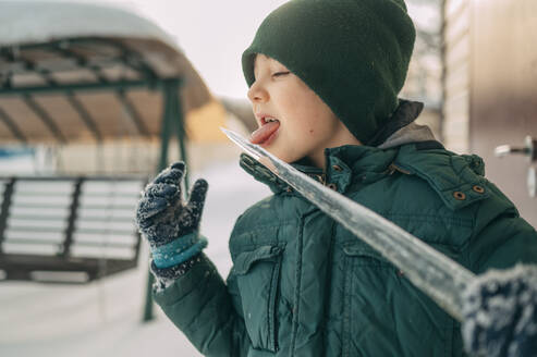 Schelmischer Junge leckt Eiszapfen im Winter - ANAF02736