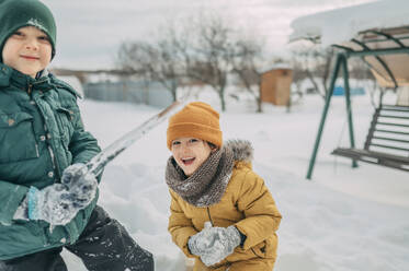 Fröhliche Geschwister spielen mit Eiszapfen im Schnee - ANAF02739