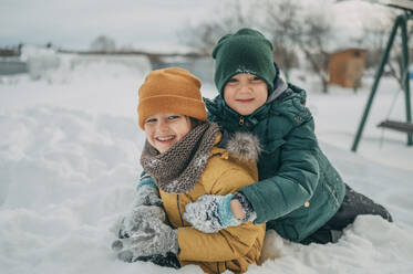 Glückliche Brüder tragen warme Kleidung und spielen im Schnee - ANAF02740