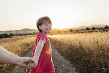 Happy girl holding father's hand and walking in field at sunset - ELMF00032
