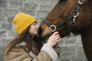 Frau küsst braunes Pferd vor einer Mauer - KVBF00042