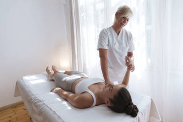 Patient lying down and getting physical therapy by osteopath in treatment room - AAZF01581