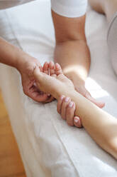 Osteopath treating pressure points on patient's palm in treatment room - AAZF01595