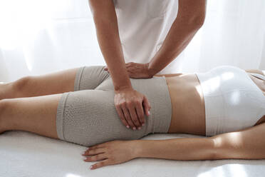 Osteopath massaging teenage patient's pelvis in treatment room - AAZF01602