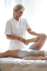 Osteopath stretching and treating patient's leg in treatment room - AAZF01605