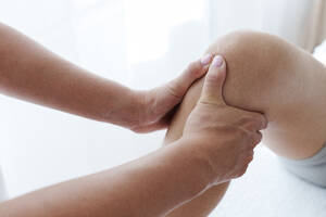 Physiotherapeutin bei chiropraktischer Anpassung am Bein eines Patienten im Behandlungsraum - AAZF01613
