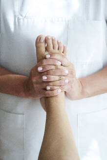 Osteopath hält und massiert den Fuß eines Patienten im Behandlungsraum - AAZF01624