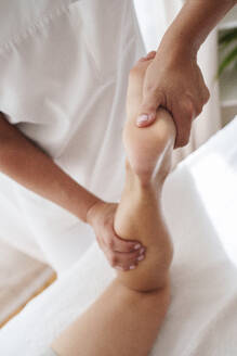 Osteopath massiert die Wade eines Patienten im Behandlungsraum - AAZF01640