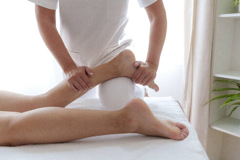 Physiotherapeutin bei der Anwendung chiropraktischer Techniken am Bein eines Patienten im Behandlungsraum - AAZF01644