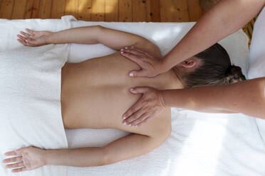 Osteopath massaging patient's back in treatment room - AAZF01654