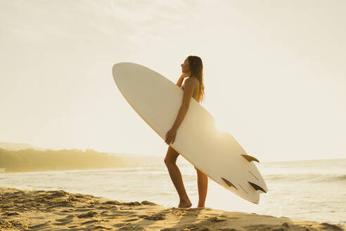 Young woman standing with surfboard at beach - AAZF01661