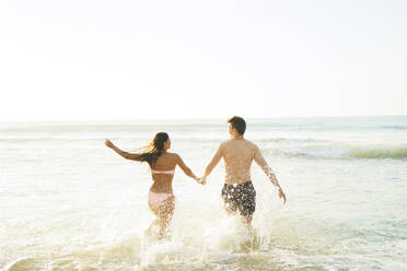 Unbeschwertes Paar hält sich an den Händen und läuft im Wasser am Strand - AAZF01663