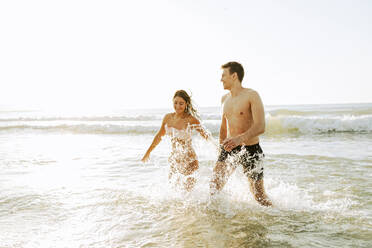 Glückliches Paar spielt im Wasser am Strand - AAZF01664