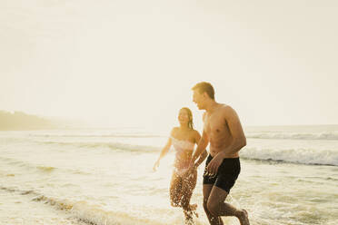 Fröhliches junges Paar spielt im Wasser am Strand - AAZF01665
