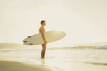 Man holding surfboard and looking at sea - AAZF01669