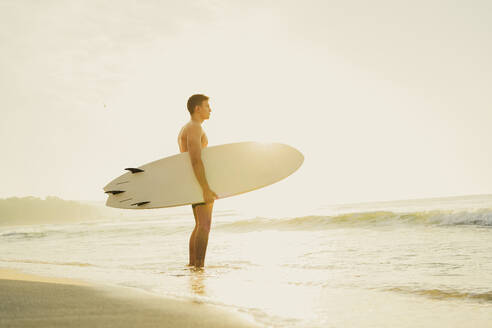 Mann hält Surfbrett und schaut aufs Meer - AAZF01669
