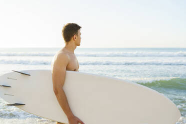 Junger Mann mit Surfbrett und Blick auf das Meer - AAZF01671