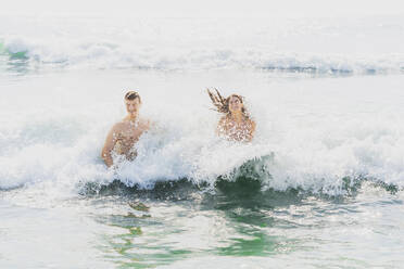 Playful couple having fun in water at beach - AAZF01676