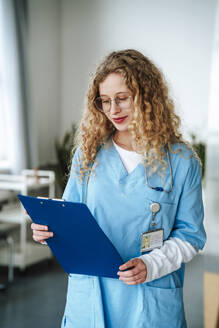 Smiling doctor reading medical document at hospital - MDOF01858