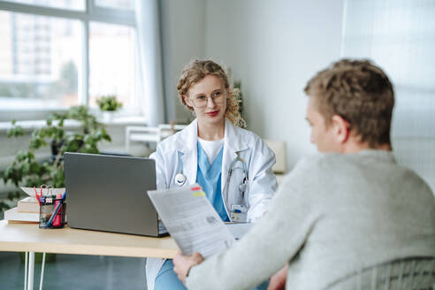 Doctor giving advice to patient reading medical report in clinic - MDOF01875