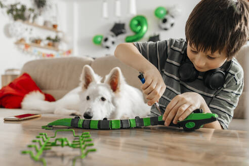 Boy assembling toy snake model near dog at home - ELMF00042