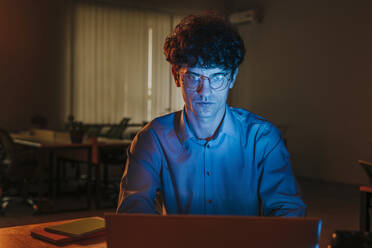 Serious businessman working on laptop in dark - YTF01892