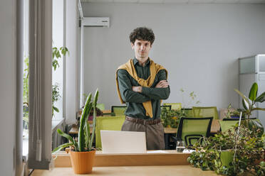 Confident businessman standing with arms crossed in office - YTF01898