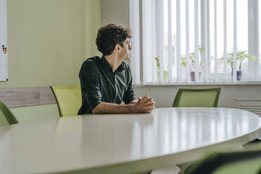 Thoughtful businessman with hands clasped sitting at table in office - YTF01917