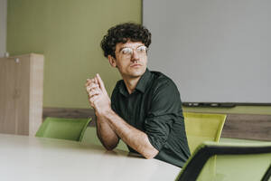 Businessman with hands clasped sitting at table in office - YTF01919