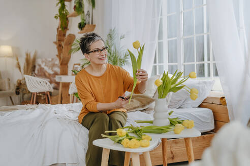 Smiling woman cutting tulips at home - YTF01929