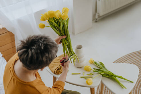 Mature woman cutting stems of tulips at home - YTF01932