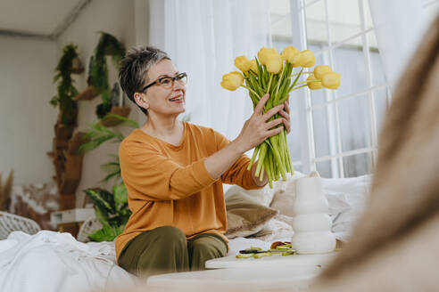 Happy woman holding bunch of tulips at home - YTF01933