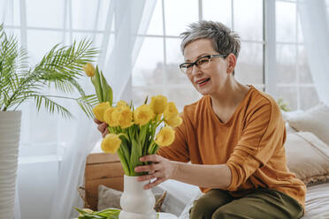 Smiling woman putting tulips in vase at home - YTF01935