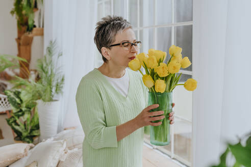 Woman smelling bunch of tulips at home - YTF01945