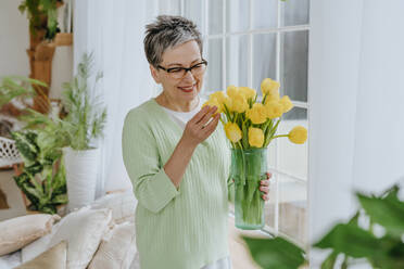 Smiling woman holding tulips in vase at home - YTF01946