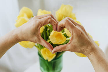 Hands of mature woman making heart over tulips at home - YTF01947