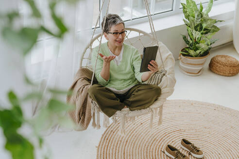 Happy woman having video call through tablet PC on hanging chair at home - YTF01953