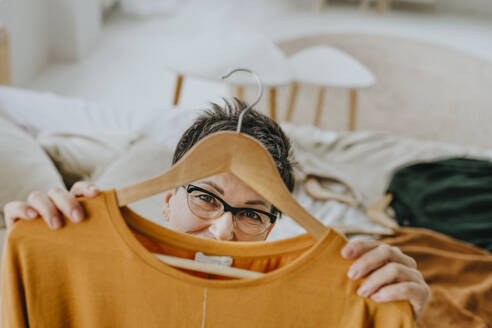 Woman wearing eyeglasses and looking through hanger at home - YTF01959