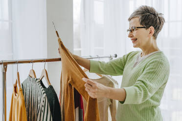 Woman choosing clothes from rack at home - YTF01960