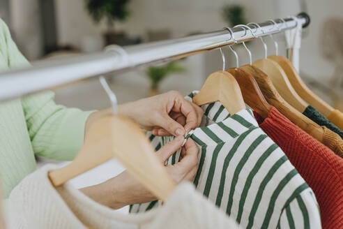 Hands of woman choosing clothes from rack at home - YTF01962